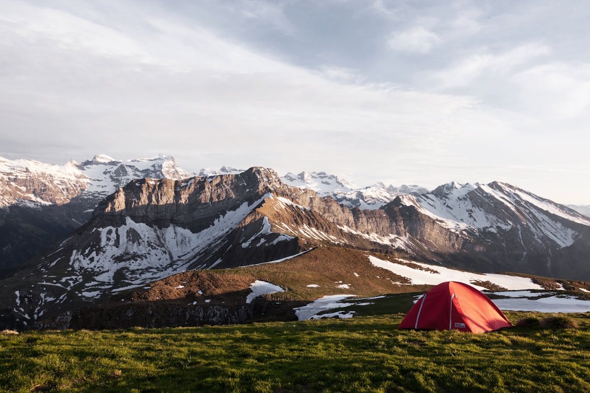 A red tent on a grass field below a snow-capped mountain - solo camping navigation skills